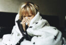 A blond child wrapped in a duvet blows their nose