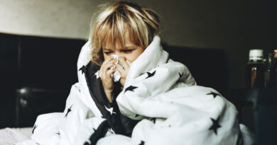 A blond child wrapped in a duvet blows their nose