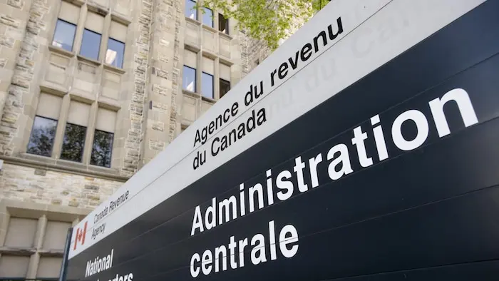 Une affiche de l'Agence du revenu du Canada devant un édifice de pierre.