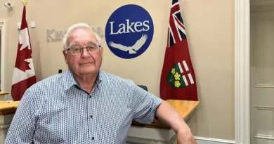 Le maire pose pour une photo dans les bureaux de la municipalité, devant une enseigne avec le nom.