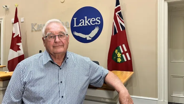 Le maire pose pour une photo dans les bureaux de la municipalité, devant une enseigne avec le nom.