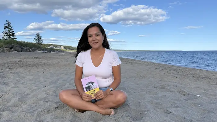 Une femme assise sur la plage et tenant un livre dans ses mains.