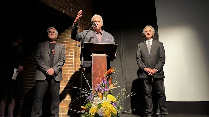Louis Dallaire, Jacques Matte et Guy Parent sur la scène du Théâtre du Cuivre, Jacques Matte gesticulant derrière le micro.