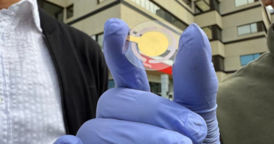 Une main gantée tient un petit capteur flexible et transparent, orné de motifs circulaires dorés.